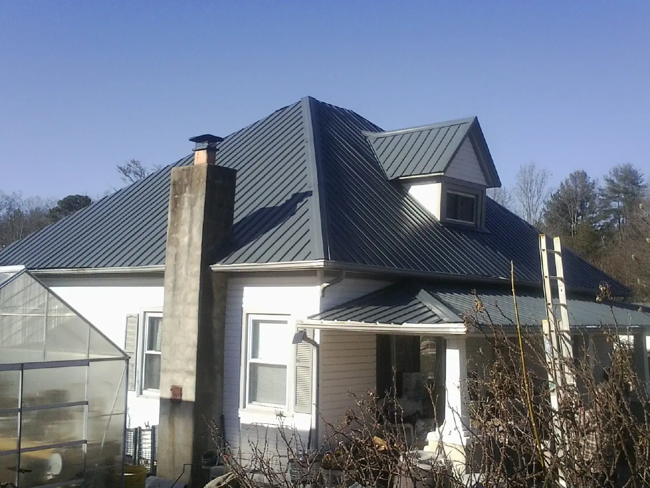 Dark blue standing seam metal roof on a white farmhouse with dormer — Slate & Tile Roof Repair by Roofing Brothers in Winnie