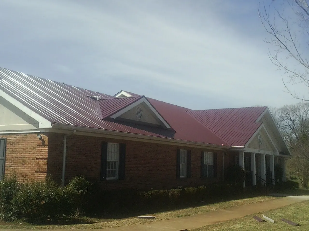 Red metal roof with gabled entries on a long brick building, from a Hail Damage Roof Repair job in Winnie