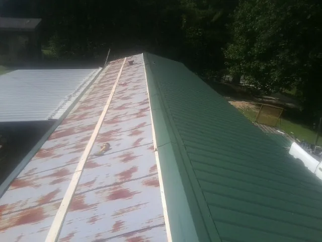 Old rusted panels beside newly installed green metal roofing — Wind Damage Roof Repair by Roofing Brothers in Winnie