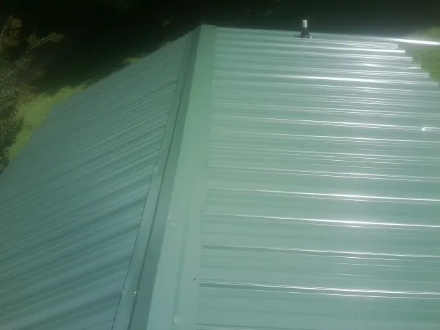New green metal panels meeting at the ridge of a roof — Flat Roof Repair work by our crew in Winnie