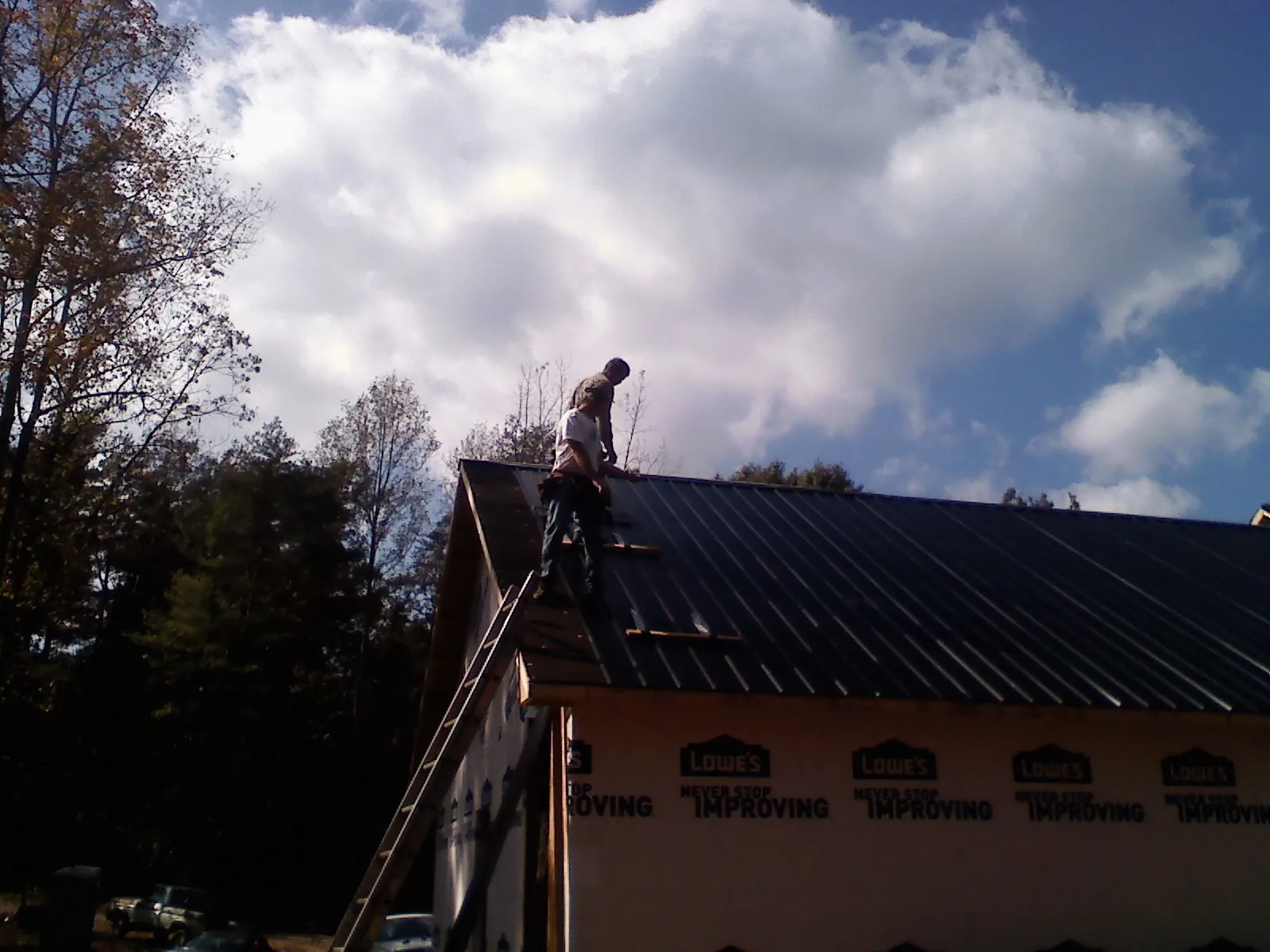 Roofer fastening dark metal panels high against a cloudy sky, from a Roof Inspection job in Winnie