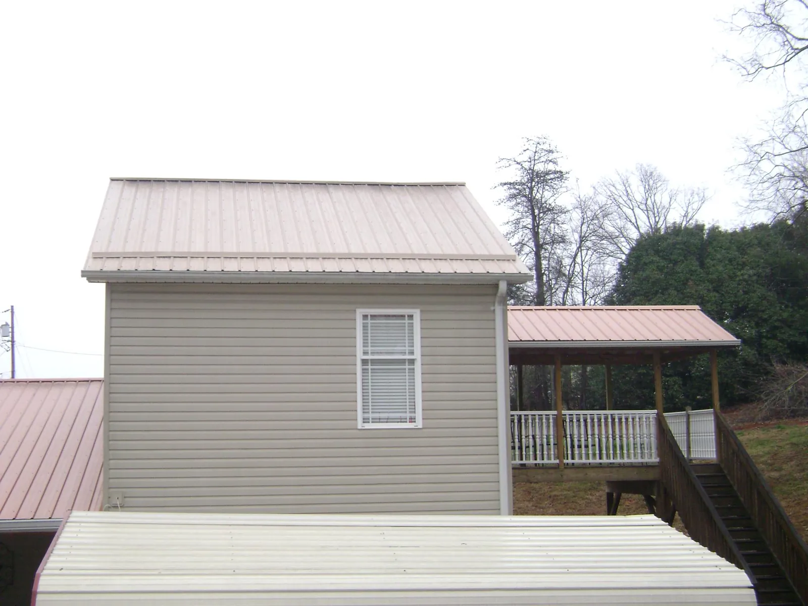 Tan metal roofs on a two story addition and attached porch, from a Roof Replacement job in Winnie
